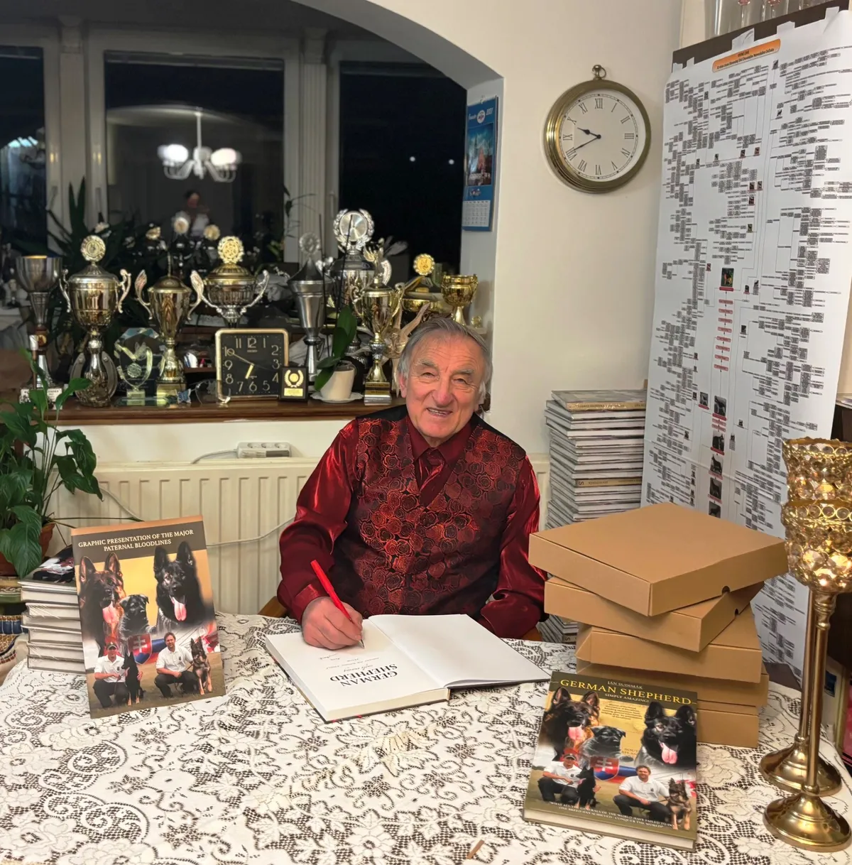 Ján Sudimák signing copies of his book at home, among trophies and a bloodline chart